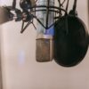 Close-up of a condenser microphone with pop filter in a studio setting, ideal for audio and podcasting.