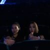 Two women sitting in a dark cinema, enjoying popcorn and watching a movie.