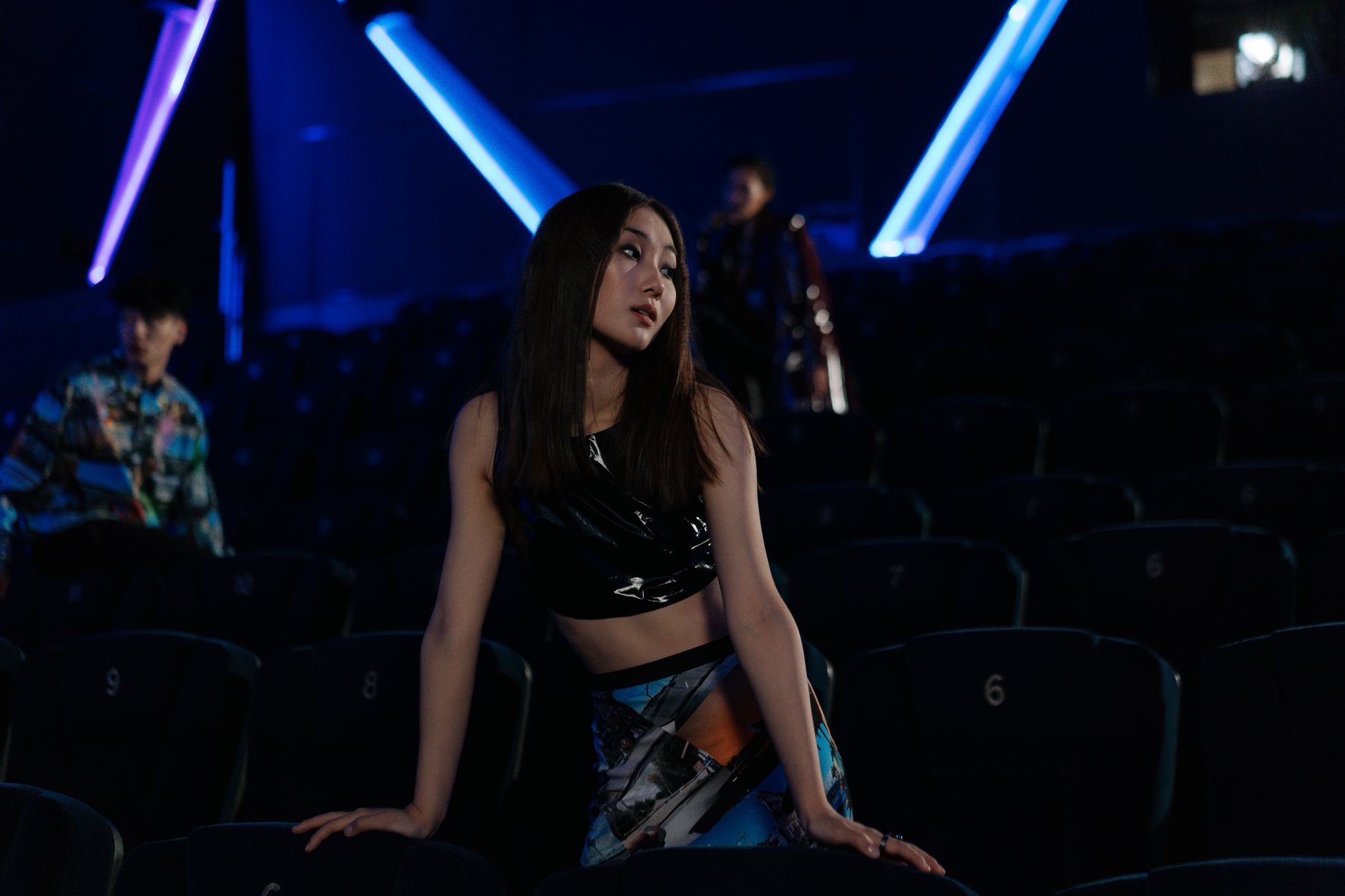 Stylish woman posing in a dimly lit cinema with neon lights and empty seats.