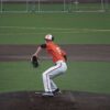 A baseball player in action, pitching on a sports field wearing an orange jersey.