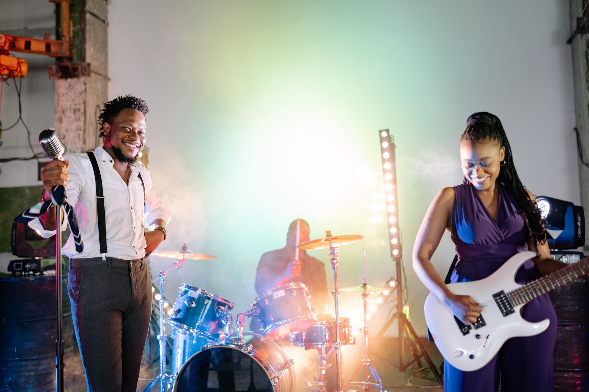 A vibrant live band performance featuring a singer, guitarist, and drummer on stage with colorful lighting.