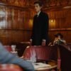 A man in a suit stands confidently in a vintage-style lounge with wooden panels and elegant decor.