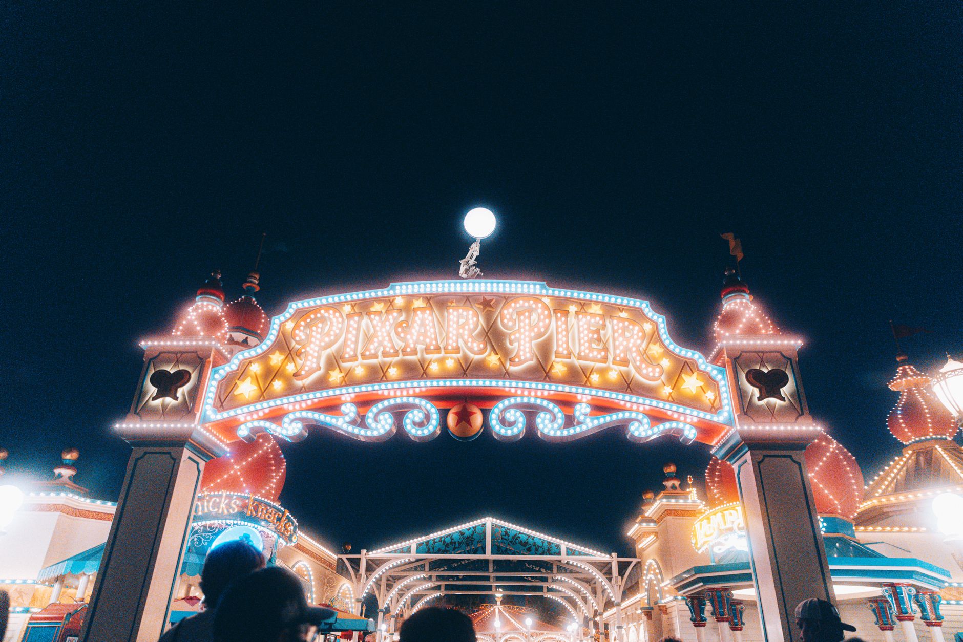 Brightly lit entrance to Pixar Pier at night, showcasing vivid carnival lights.